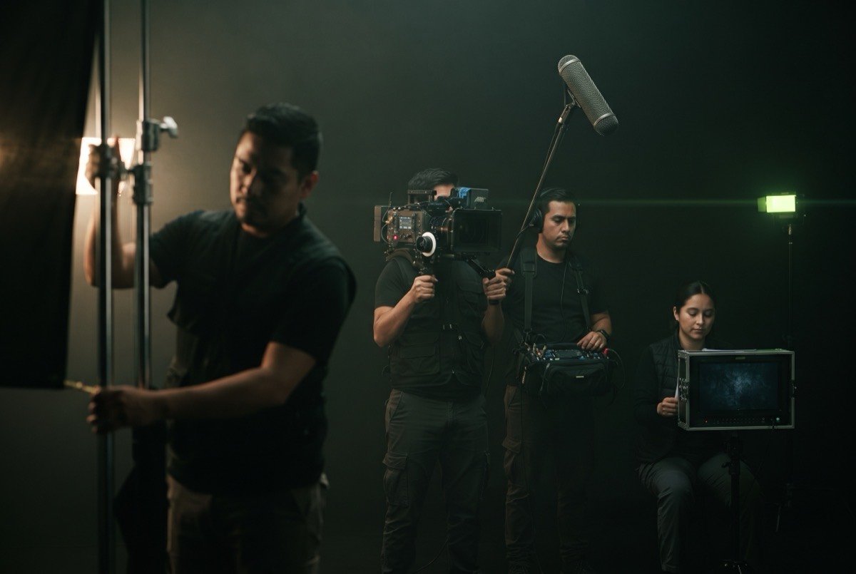 Equipo de producción trabajando en set: cámara, boom de audio, iluminación y monitoreo
